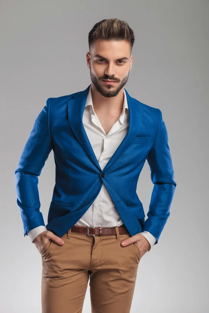 Casual Spring Fashion in New York American Man with beard wearing white  shirt tan pants sneakers blue sweater put around shoulder holding cell  phone sitting on street with vintage building Stock Photo 