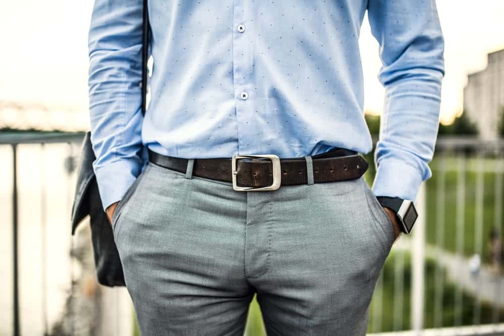 Dressing in a blue shirt gray pants and black leather shoes one hand  touching his chin