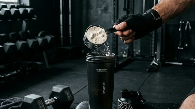 Man scooping protein powder into shaker at gym